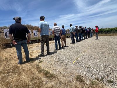 People practicing shooting at an outdoor gun range under a clear sky.