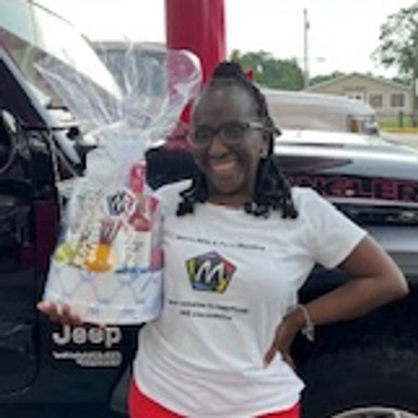 Jarmele Fairclaugh wearing a white short sleeve T-Shirt holding a Bridal Shower Gift Basket in front
