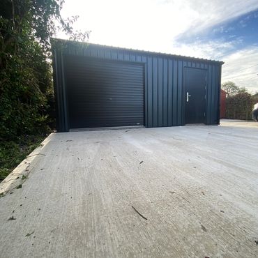A modern black metal garage with a roller door and side entry door on a concrete driveway.