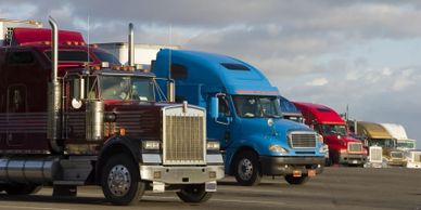 A lineup of colorful semi-trucks parked under a cloudy sky.
