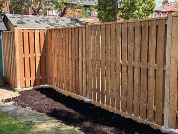 Freshly installed wooden fence with a garden bed beside it in a backyard.