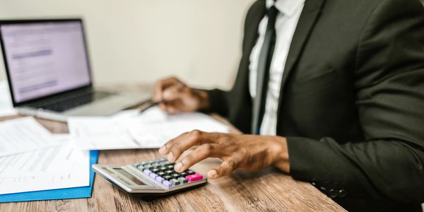 Man sitting at desk with laptop, reviewing papers and entering numbers on a calculator.  