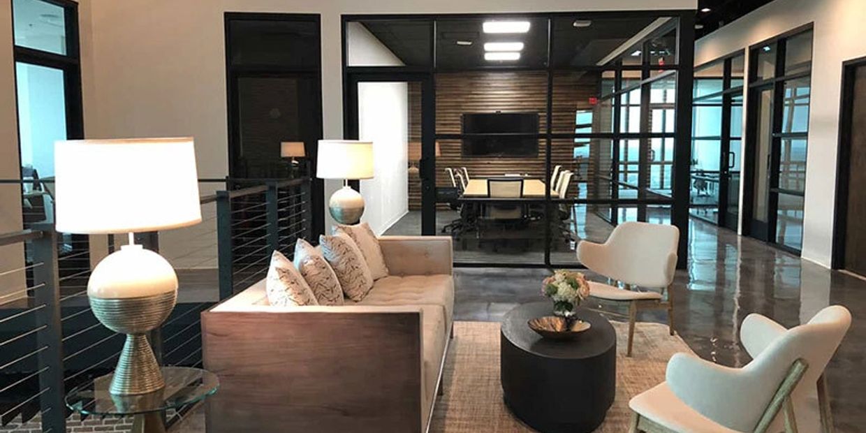 Modern office lounge area with sofa, chairs, and lamps.