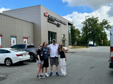 Four people posing in front of Second Harvest Food Bank building on a sunny day.