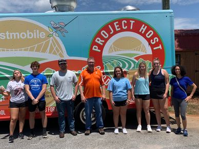 Group of eight people standing in front of a colorful Project Host food truck.