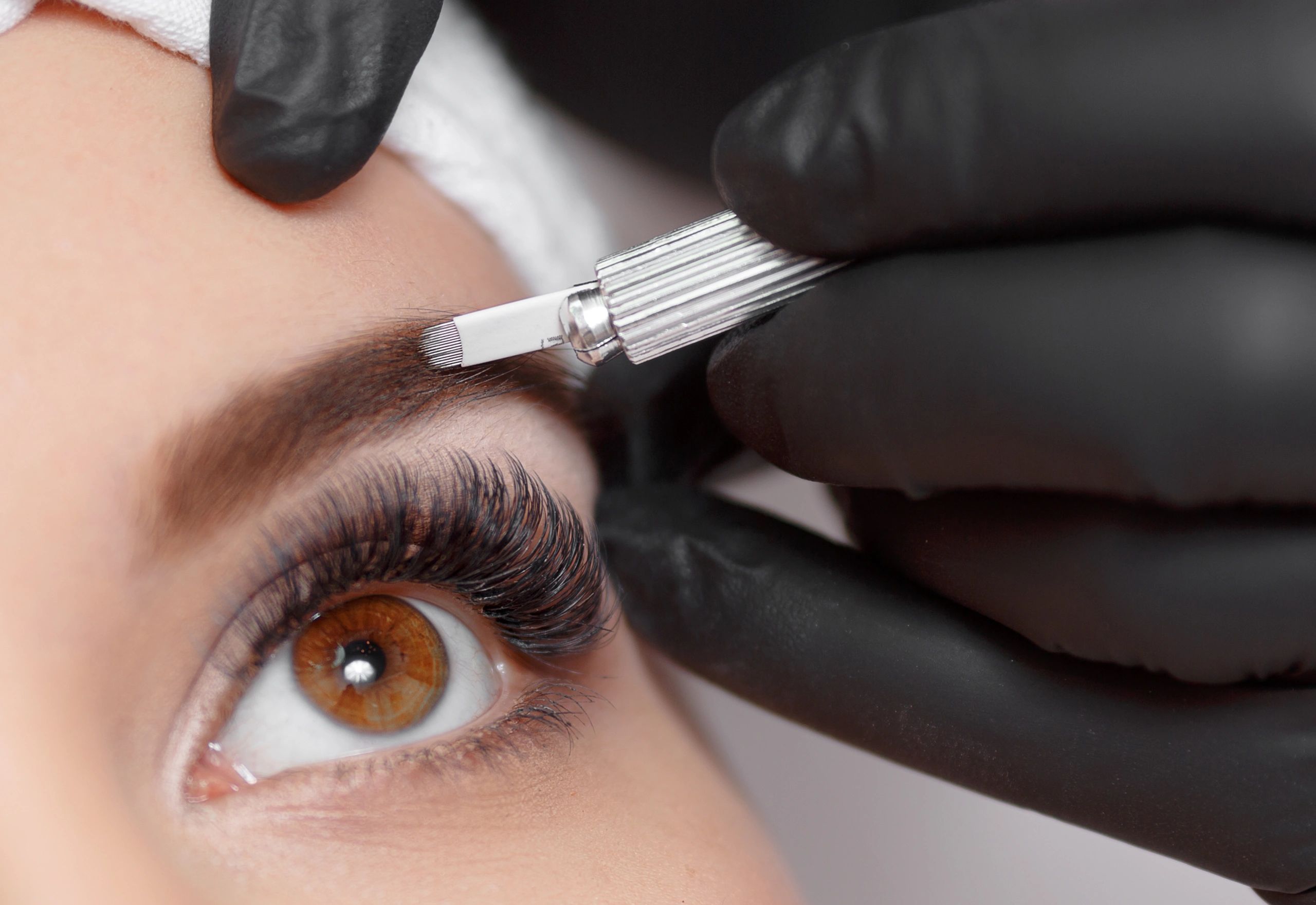 Close-up of a technician performing microblading with gloved hand and tool