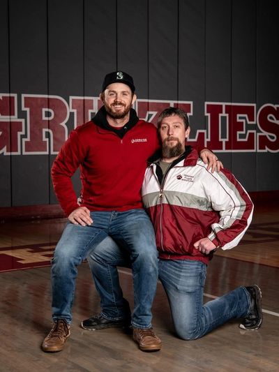 Two men posing inside a gym with "GRIZZLIES" text behind.