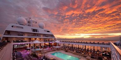 Luxurious cruise ship deck with pool at sunset under vibrant sky.