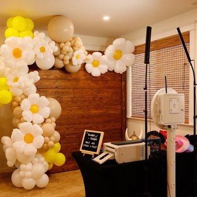 Photo booth setup with daisy-themed balloon arch and wooden backdrop.