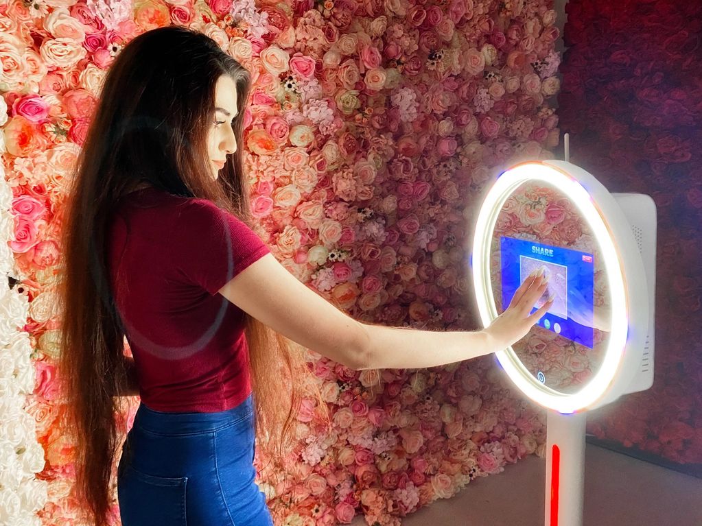 Woman using a touchscreen photo booth with floral backdrop.