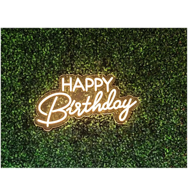 Illuminated "Happy Birthday" sign on a green leafy background.