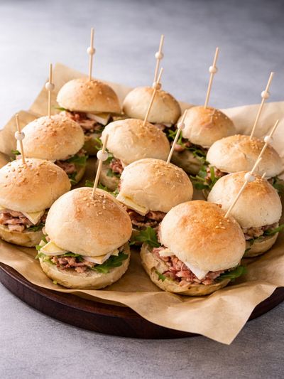 Tray of mini sandwiches with lettuce and meat, each secured with a skewer.
