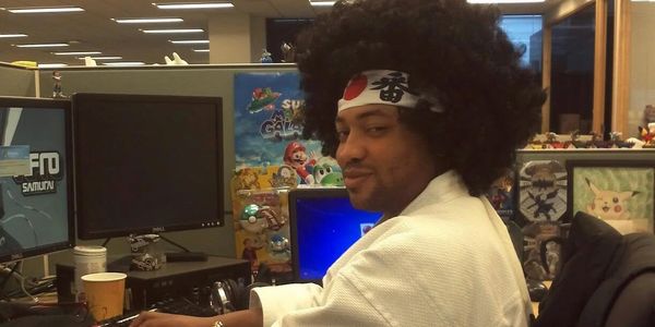 Man with afro and headband sitting at a computer desk.