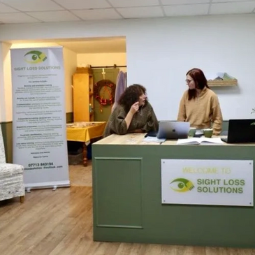 Two people standing behind the Sight Loss Solutions reception desk. 