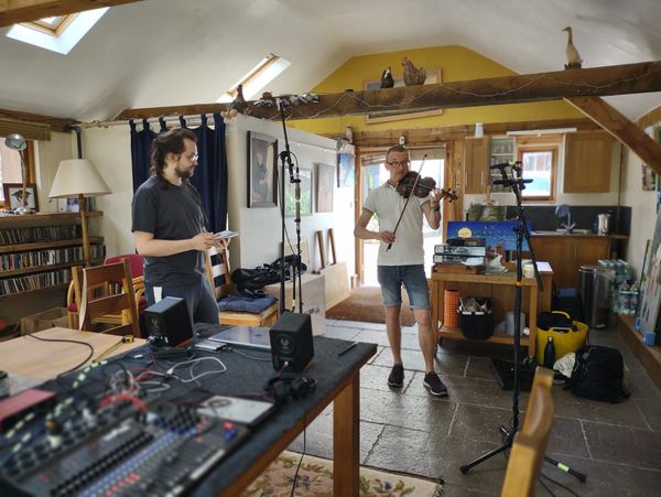 Two men in a cozy room with musical instruments and recording equipment.
