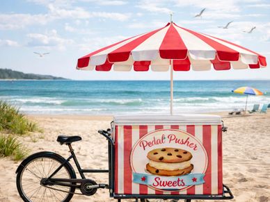 A red-and-white striped ice cream bike on a sunny beach with ocean waves.