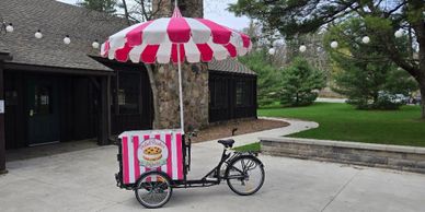 A tricycle with a pink and white umbrella and a pizza-themed box attached.