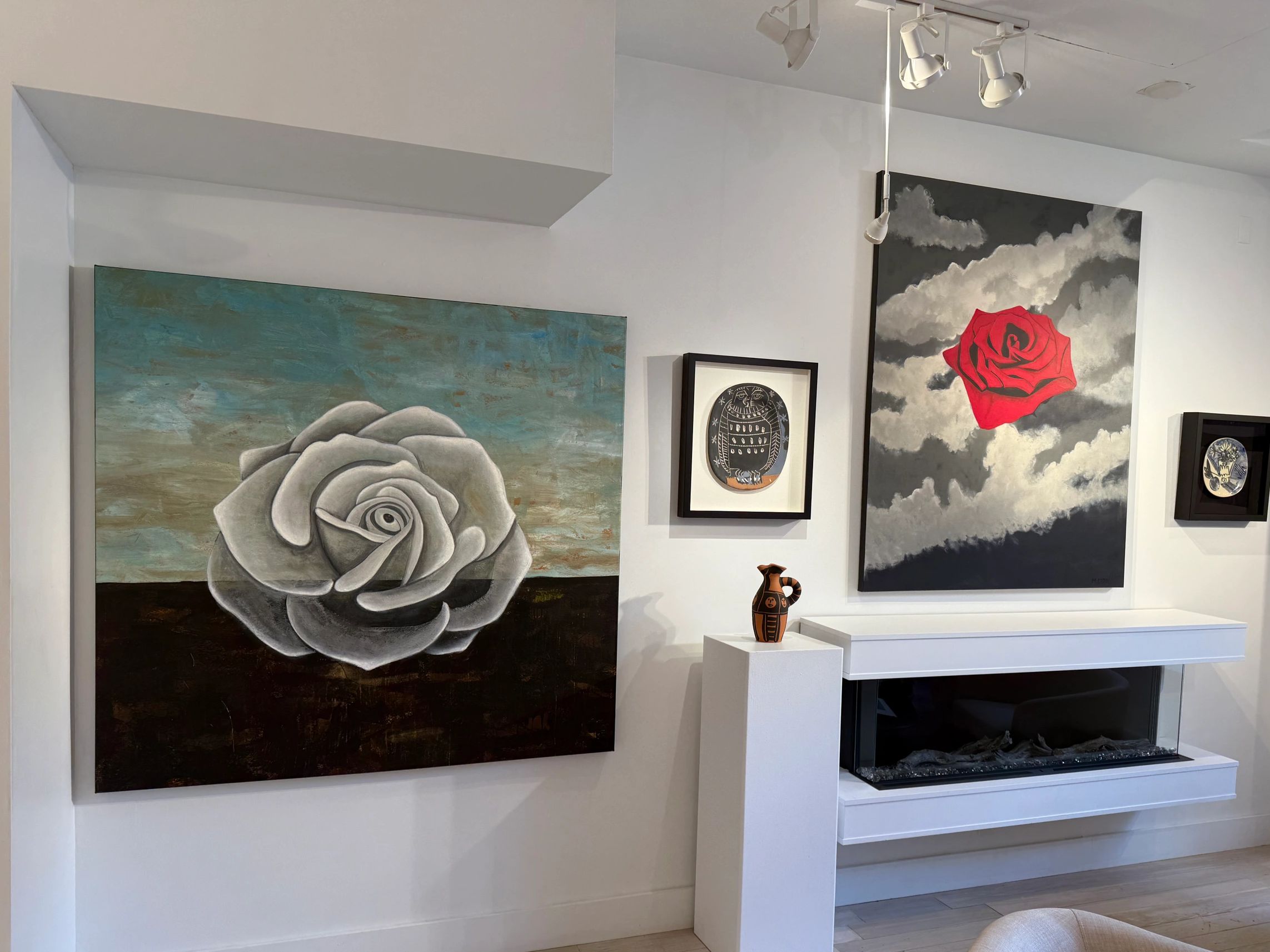 Gallery wall with paintings of roses and owl, ceramic vase on pedestal.