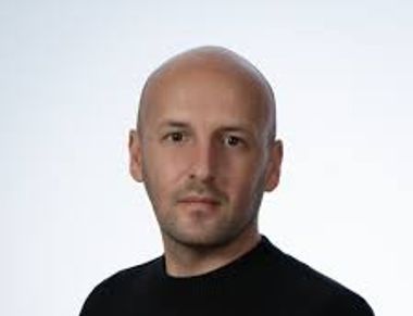 Portrait of a bald man in a black shirt against a plain background.