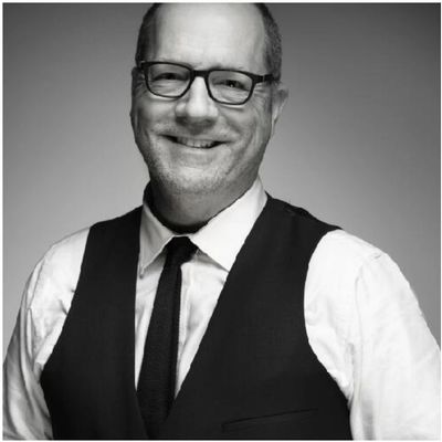 Smiling man in glasses and vest.