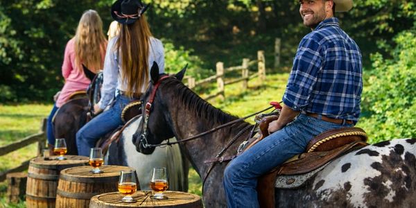 People enjoying horseback riding with drinks on barrels outdoors.