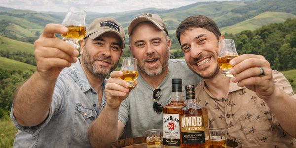 Three men cheer with glasses of whiskey outdoors with scenic hills.