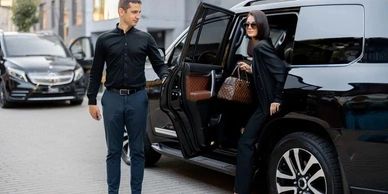 A stylish woman exits a black SUV while a man holds the door open.