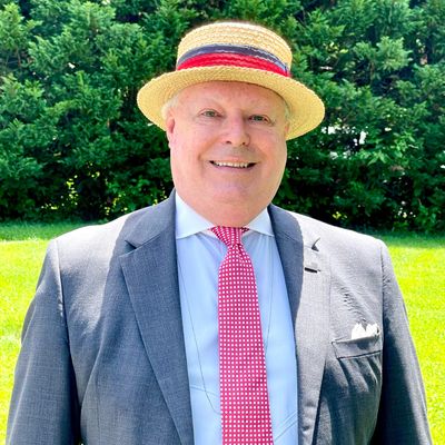 Dr. Ryan is pictured smiling. He is wearing a grey suit and a boater hat. 