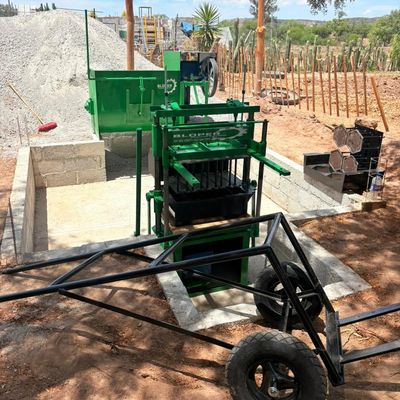 Green concrete block making machine set up outdoors on a construction site.