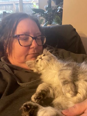 Woman wearing glasses cuddling a fluffy cat on a couch.