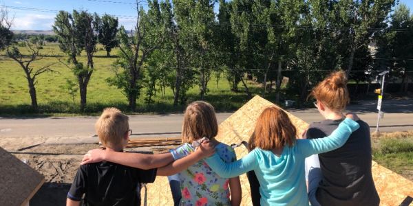Four children sitting with arms around each other outdoors.