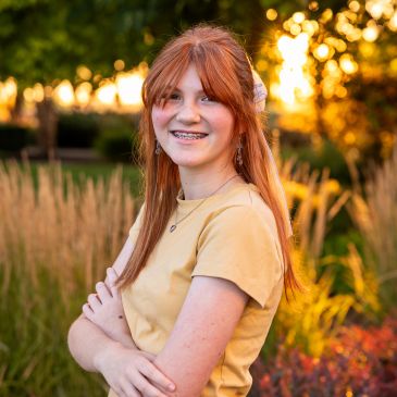 Young red-haired woman smiling outdoors at sunset.