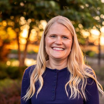 Smiling woman with long blonde hair outdoors at sunset.