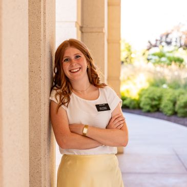 Smiling woman leaning against wall outdoors.