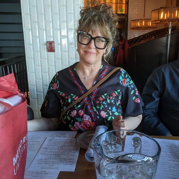 Woman with glasses sitting at a restaurant table with menus and a water pitcher.