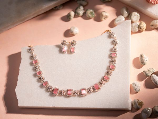Elegant pink gemstone necklace with matching earrings on a marble slab.