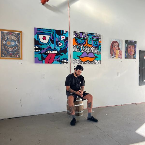 Man sitting on a barrel in an art gallery with colorful paintings on the wall.