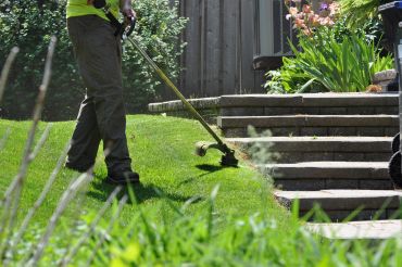 Person using a string trimmer to cut grass near steps.