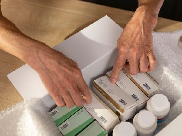 A close-up of a person's hands packing boxes of medication and pill bottles into a box.

