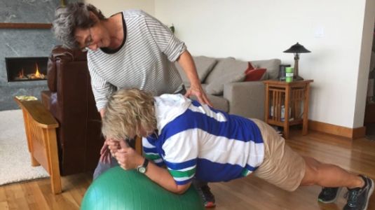 Fitness trainer Shirley Champoux guides woman in plank position on exercise ball