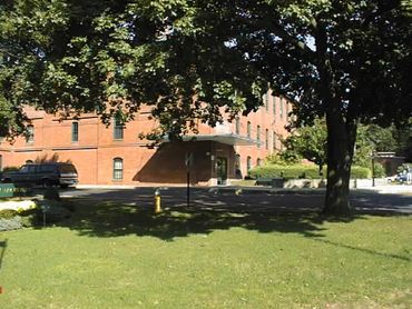 A brick building with trees and a green lawn in front.