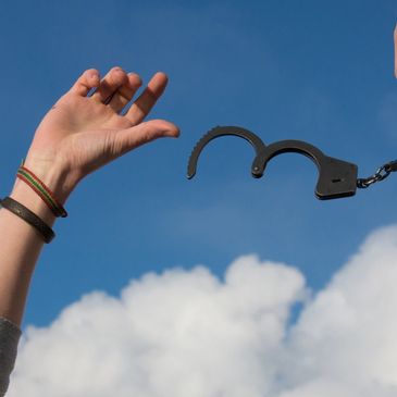 Hands breaking free from handcuffs against a blue sky.