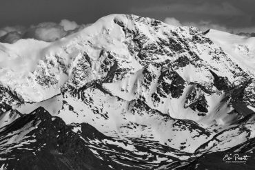 Black and white image of a snow-covered mountain peak with rugged terrain.
