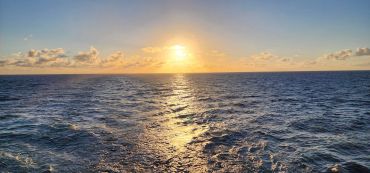 Sunset over the ocean with shimmering water and scattered clouds.