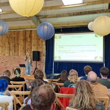 A speaker presents to an attentive audience in a rustic hall.