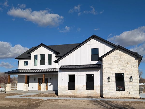 Modern white house with black roof and stone accents under a blue sky.