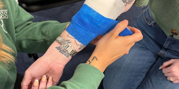 Person wrapping blue bandage on another's wrist.