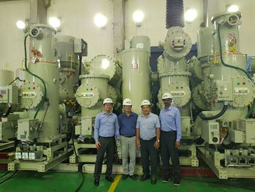 Four men in helmets stand in front of large industrial machinery.