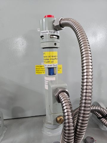 Close-up of an industrial pressure relief device with metal tubing and warning labels.