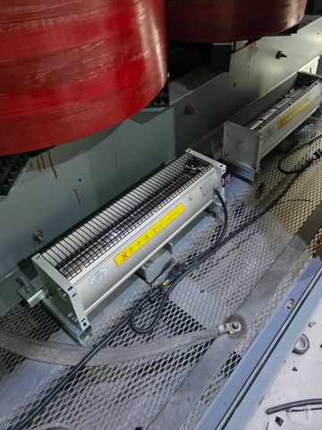 Industrial electrical coils with warning labels on a metal platform.